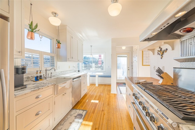 kitchen with pendant lighting, sink, white cabinetry, stainless steel appliances, and ventilation hood