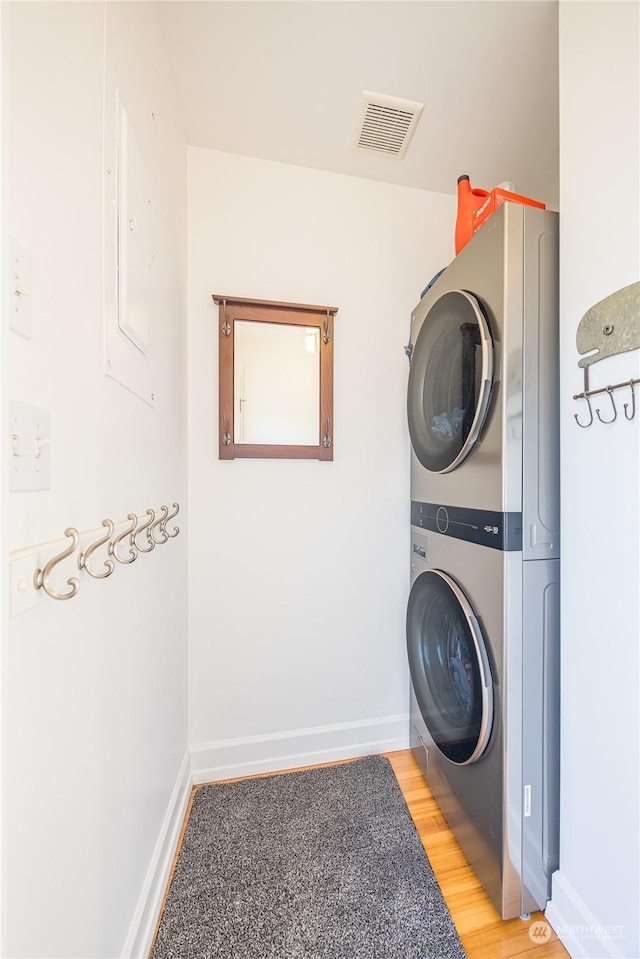 laundry room featuring stacked washer and dryer and wood-type flooring