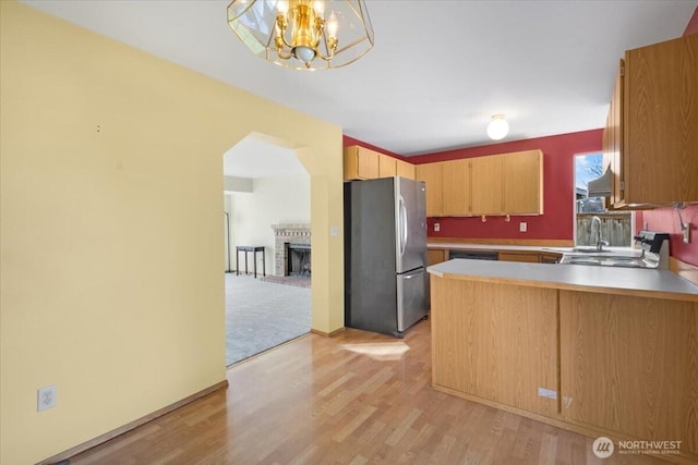 kitchen featuring hanging light fixtures, light wood-type flooring, stainless steel fridge, kitchen peninsula, and a fireplace