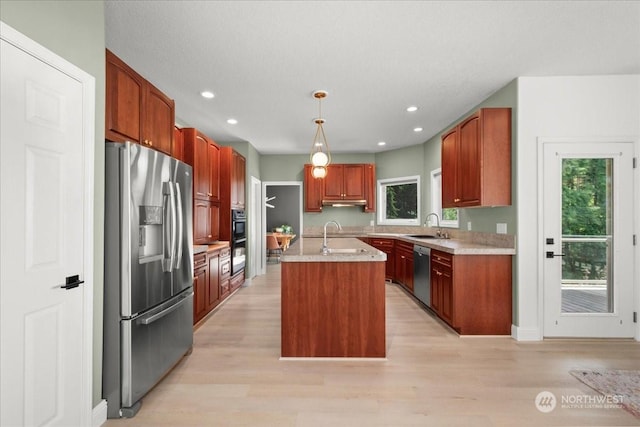 kitchen with sink, appliances with stainless steel finishes, a kitchen island with sink, decorative light fixtures, and light wood-type flooring