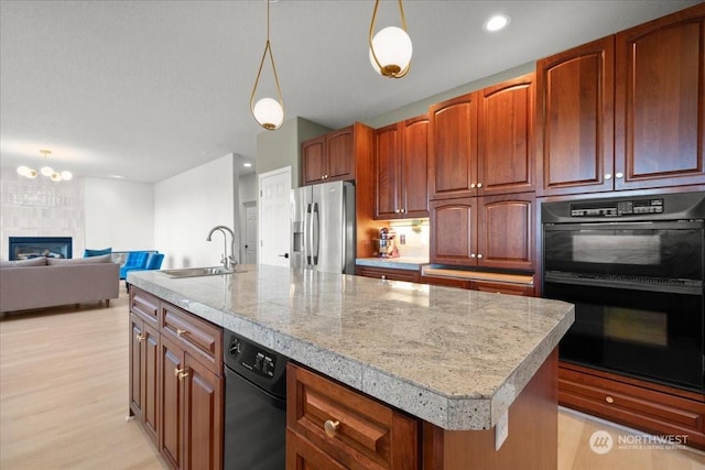 kitchen with sink, black double oven, a center island with sink, stainless steel fridge with ice dispenser, and decorative light fixtures