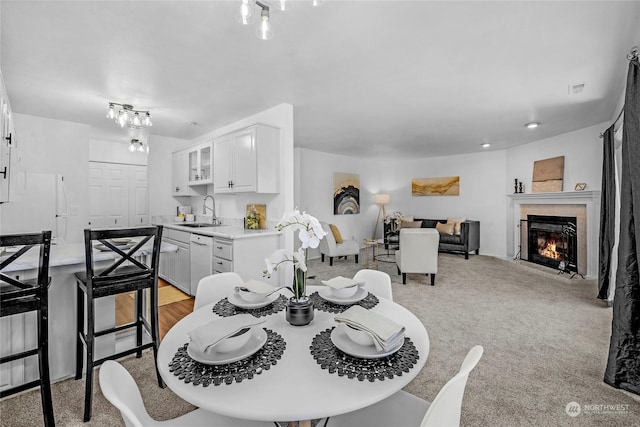 dining space with a tiled fireplace, sink, and light colored carpet