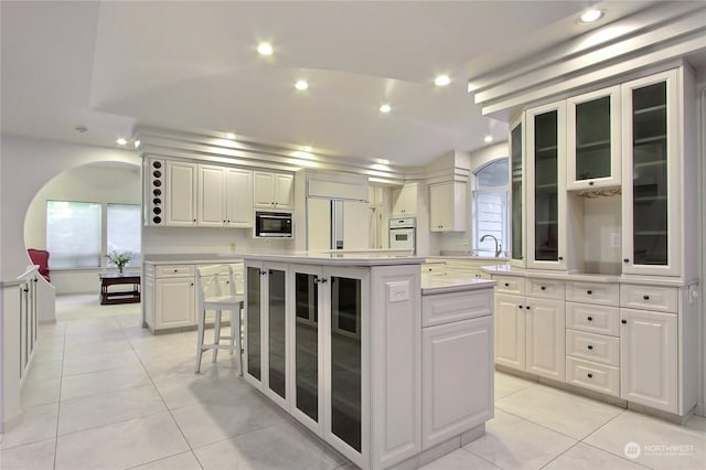 kitchen featuring built in appliances, light tile patterned floors, a center island, and white cabinets