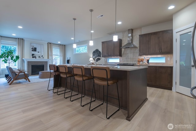 kitchen featuring a breakfast bar, visible vents, light wood-style flooring, and wall chimney exhaust hood