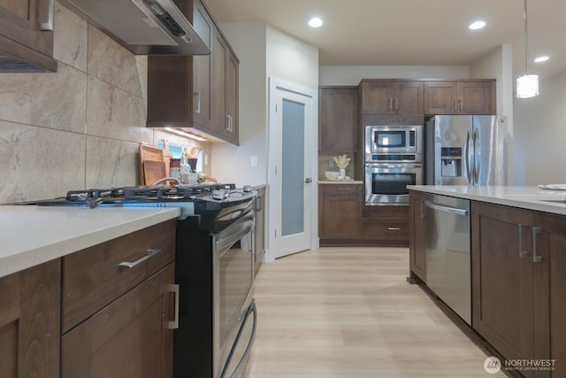 kitchen featuring range hood, stainless steel appliances, light countertops, light wood-style flooring, and backsplash