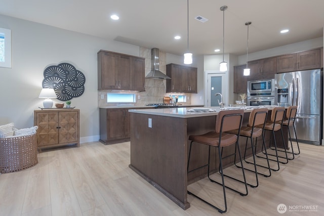 kitchen with stainless steel appliances, visible vents, light wood-style flooring, decorative backsplash, and wall chimney exhaust hood