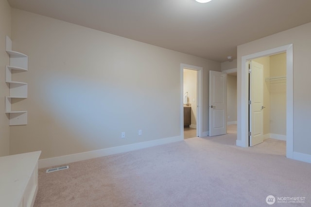 unfurnished bedroom featuring carpet floors, a walk in closet, visible vents, ensuite bath, and baseboards