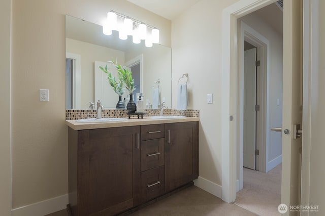 bathroom featuring baseboards, double vanity, a sink, and decorative backsplash