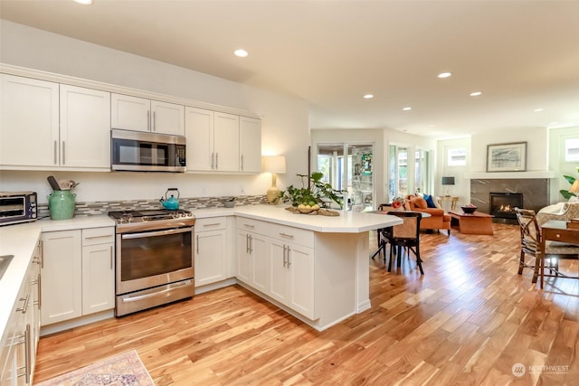 kitchen featuring light hardwood / wood-style flooring, a premium fireplace, stainless steel appliances, white cabinets, and kitchen peninsula