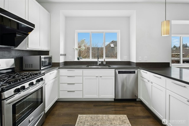 kitchen featuring white cabinets, dark countertops, appliances with stainless steel finishes, pendant lighting, and a sink