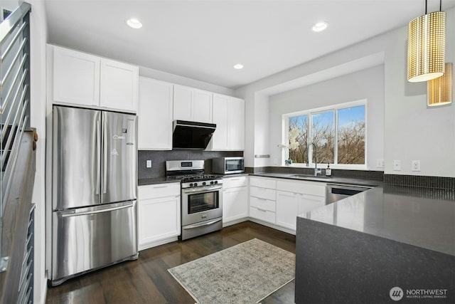 kitchen with appliances with stainless steel finishes, dark countertops, white cabinetry, and pendant lighting