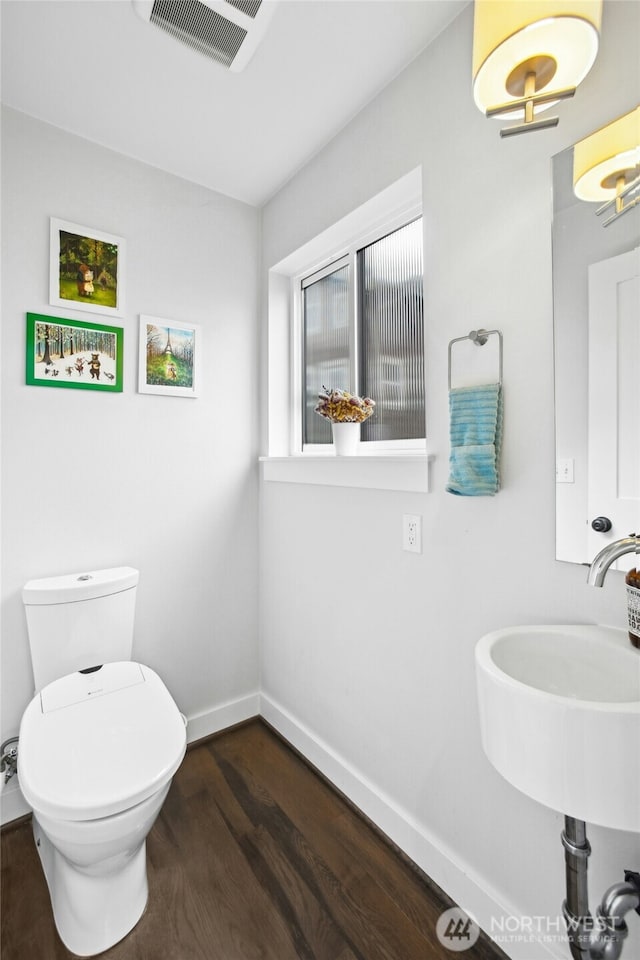 half bath featuring baseboards, visible vents, toilet, wood finished floors, and a sink