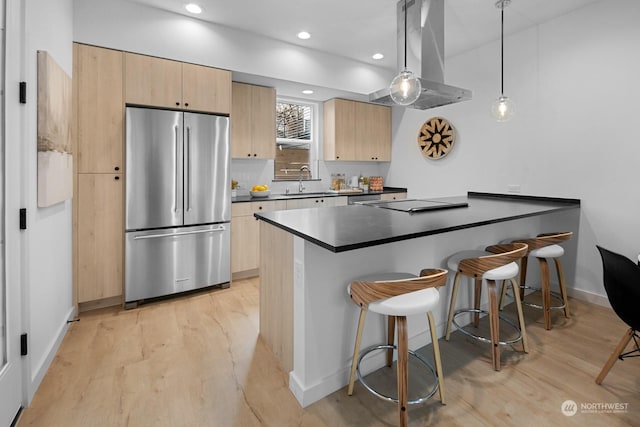 kitchen with a breakfast bar, island range hood, pendant lighting, sink, and stainless steel fridge