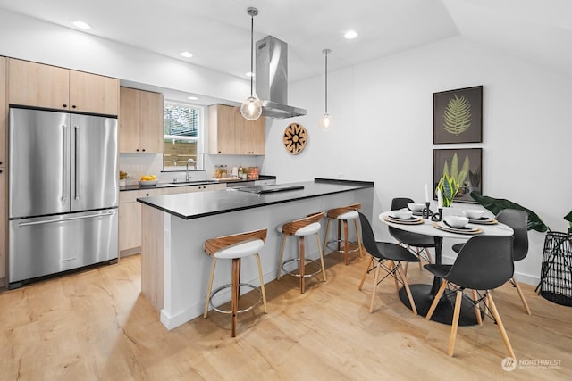 kitchen with pendant lighting, island exhaust hood, kitchen peninsula, high end fridge, and light hardwood / wood-style flooring