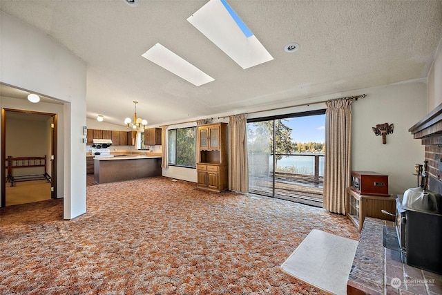 carpeted living room featuring a healthy amount of sunlight, a textured ceiling, vaulted ceiling with skylight, and an inviting chandelier