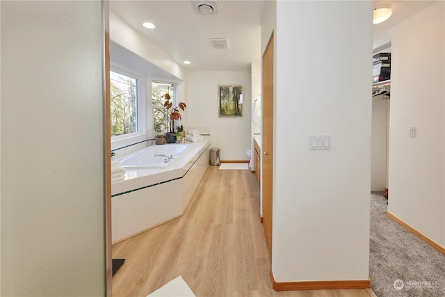 bathroom with a relaxing tiled tub, vanity, hardwood / wood-style flooring, and toilet