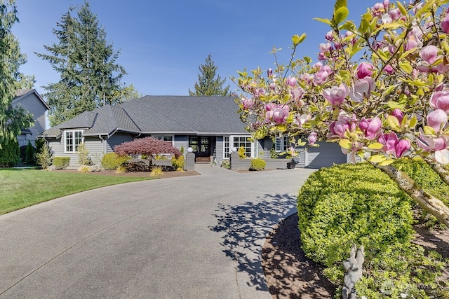 ranch-style house featuring roof with shingles, driveway, a front yard, and french doors