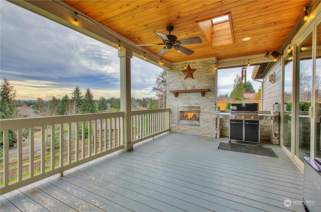 deck at dusk with ceiling fan, grilling area, and an outdoor stone fireplace