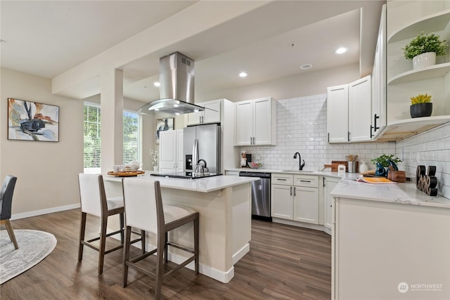 kitchen with appliances with stainless steel finishes, white cabinetry, a kitchen breakfast bar, island exhaust hood, and a kitchen island with sink