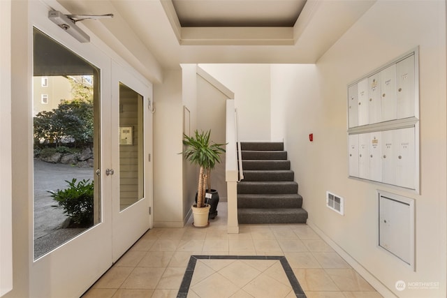 doorway featuring a raised ceiling, a mail area, and light tile patterned floors