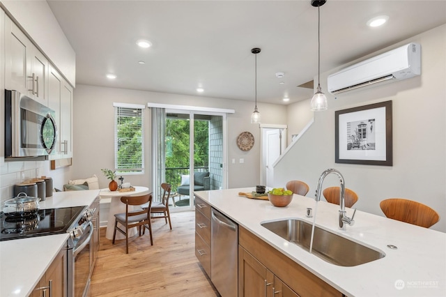 kitchen featuring pendant lighting, sink, appliances with stainless steel finishes, a wall unit AC, and light wood-type flooring