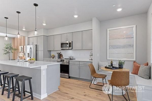 kitchen with gray cabinets, a breakfast bar, pendant lighting, sink, and stainless steel appliances