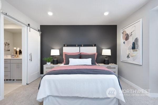 carpeted bedroom with a barn door and ensuite bath