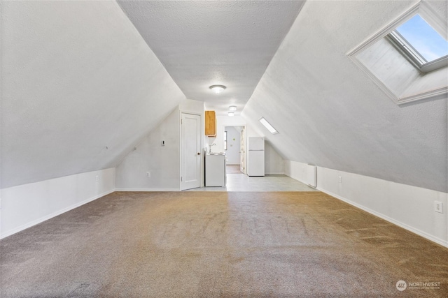 bonus room featuring lofted ceiling with skylight, washer / dryer, light colored carpet, and a textured ceiling