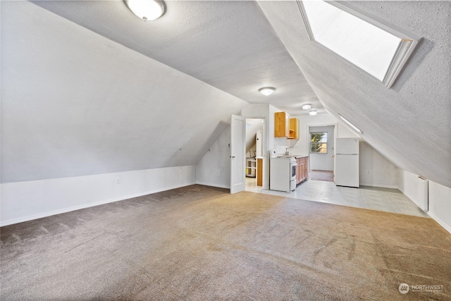 bonus room featuring vaulted ceiling with skylight, light carpet, and a textured ceiling