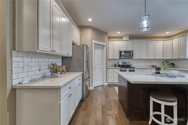 kitchen with hanging light fixtures, stainless steel appliances, dark hardwood / wood-style floors, light stone countertops, and white cabinets