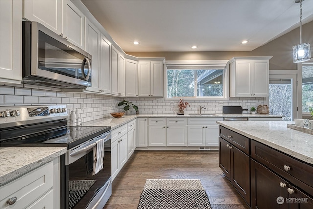 kitchen featuring appliances with stainless steel finishes, pendant lighting, white cabinetry, wood-type flooring, and light stone counters