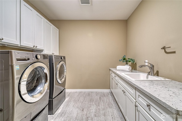 laundry area featuring cabinets, sink, washer and dryer, and light hardwood / wood-style flooring