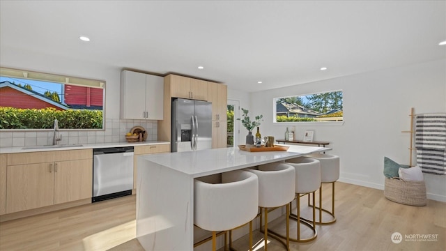 kitchen featuring a kitchen island, appliances with stainless steel finishes, sink, decorative backsplash, and light wood-type flooring