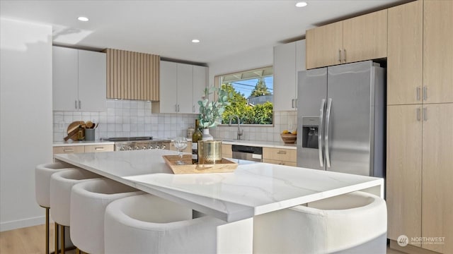 kitchen featuring a kitchen bar, a kitchen island, stainless steel appliances, light stone countertops, and decorative backsplash