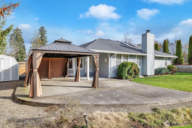 rear view of property featuring an outbuilding, a storage shed, a gazebo, a lawn, and a chimney