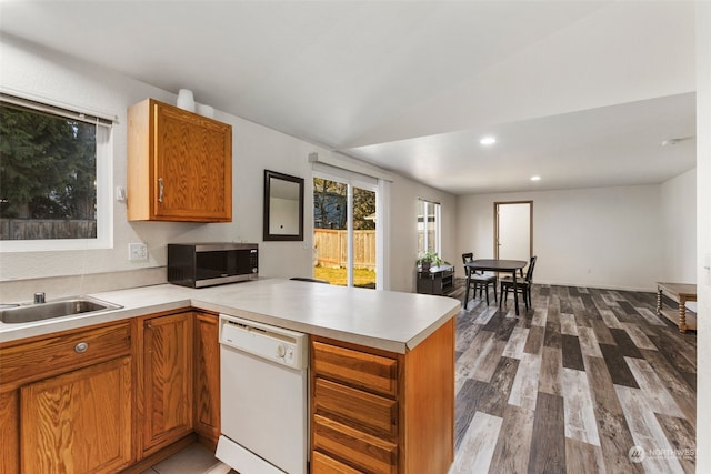 kitchen with vaulted ceiling, dishwasher, wood-type flooring, sink, and kitchen peninsula