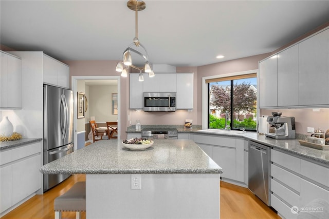 kitchen with a kitchen island, pendant lighting, white cabinetry, sink, and stainless steel appliances