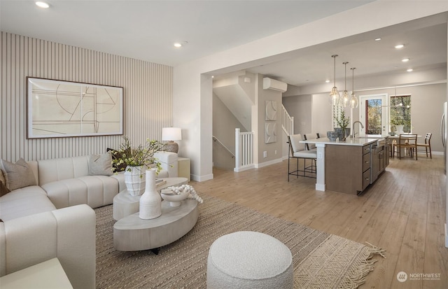 living room featuring an inviting chandelier, light hardwood / wood-style floors, sink, and a wall unit AC