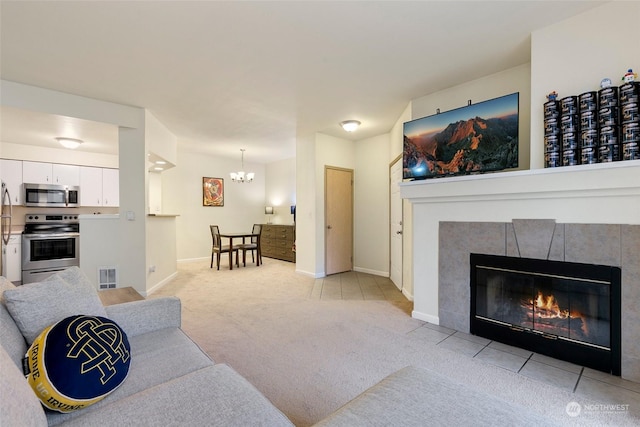 carpeted living room featuring a tile fireplace and a notable chandelier