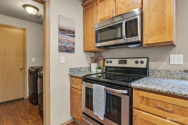 kitchen with light stone countertops, appliances with stainless steel finishes, dark hardwood / wood-style floors, and separate washer and dryer