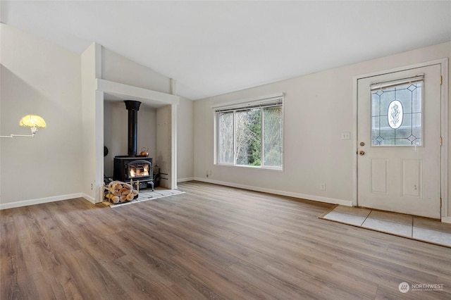 foyer featuring lofted ceiling, a wood stove, and light hardwood / wood-style floors