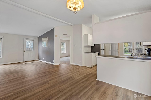 unfurnished living room with a chandelier, lofted ceiling, light hardwood / wood-style floors, and sink