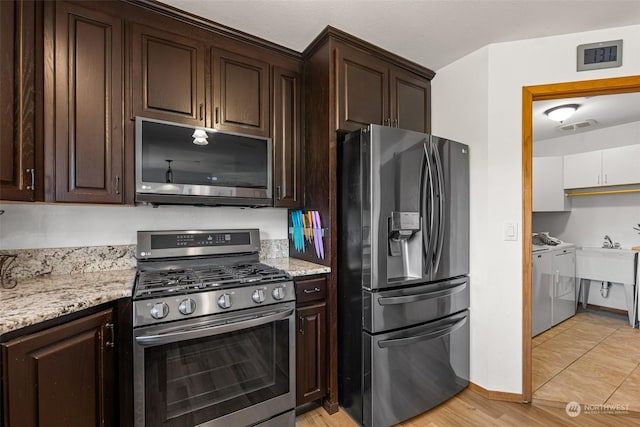 kitchen with light stone counters, stainless steel appliances, washer and clothes dryer, and dark brown cabinets