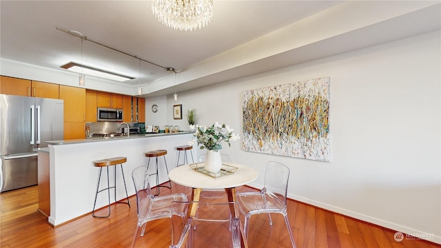 kitchen with an inviting chandelier, stainless steel appliances, kitchen peninsula, and light wood-type flooring