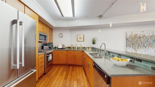 kitchen with appliances with stainless steel finishes, sink, hanging light fixtures, kitchen peninsula, and light hardwood / wood-style flooring