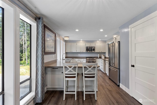 kitchen featuring a breakfast bar area, high end appliances, dark hardwood / wood-style flooring, kitchen peninsula, and white cabinets