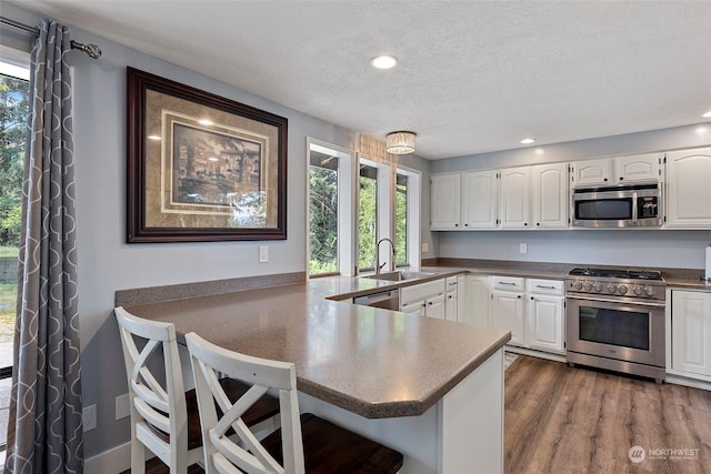 kitchen featuring sink, kitchen peninsula, white cabinets, and appliances with stainless steel finishes