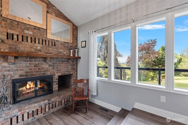 sitting room with wood-type flooring, a fireplace, vaulted ceiling, and a wealth of natural light