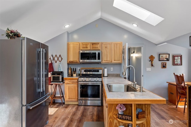 kitchen with sink, appliances with stainless steel finishes, hardwood / wood-style floors, lofted ceiling with skylight, and tile countertops