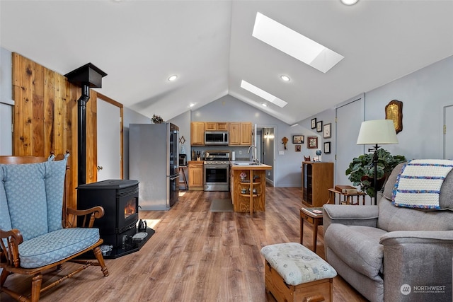 living room featuring vaulted ceiling with skylight, sink, a wood stove, and light wood-type flooring